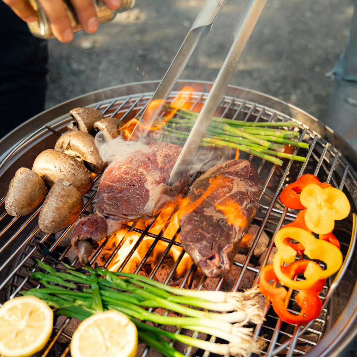 A charcoal barbecue loaded with meat, corn and peppers over the coals