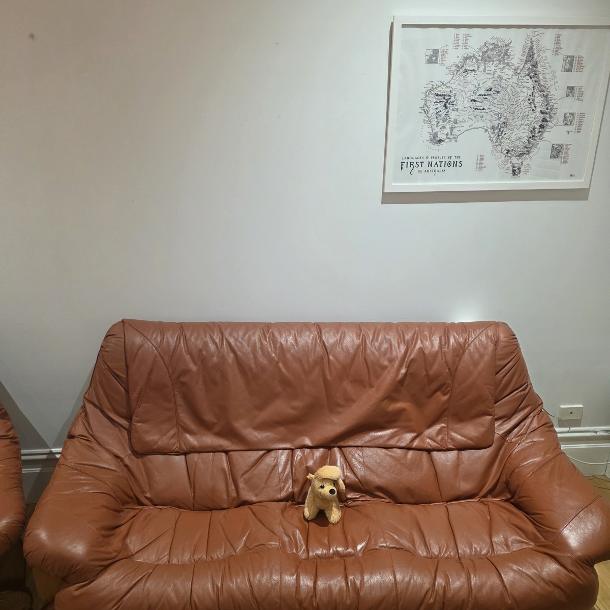 A tan leather couch against a mostly bare wall