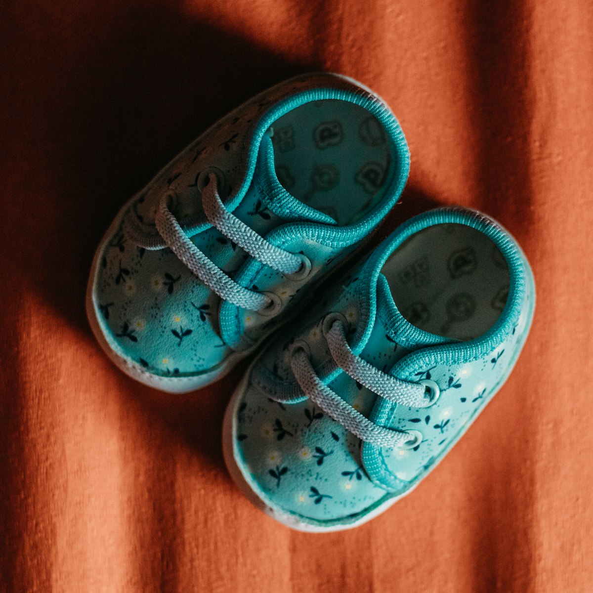 A tiny pair of teal baby shoes on a rust coloured blanket
