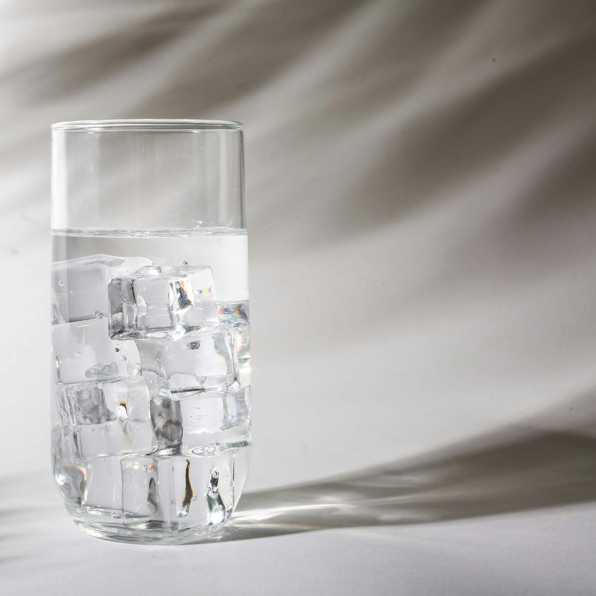 A tall glass of soda water full of ice, with soft shadows behind it
