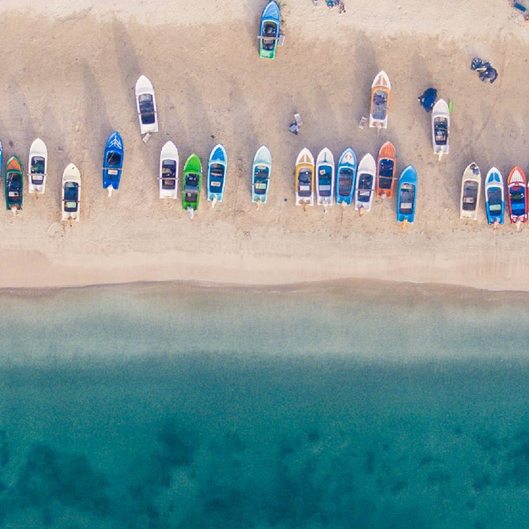 Fishing boats lined up on the sand above clear shallow water, seen from above