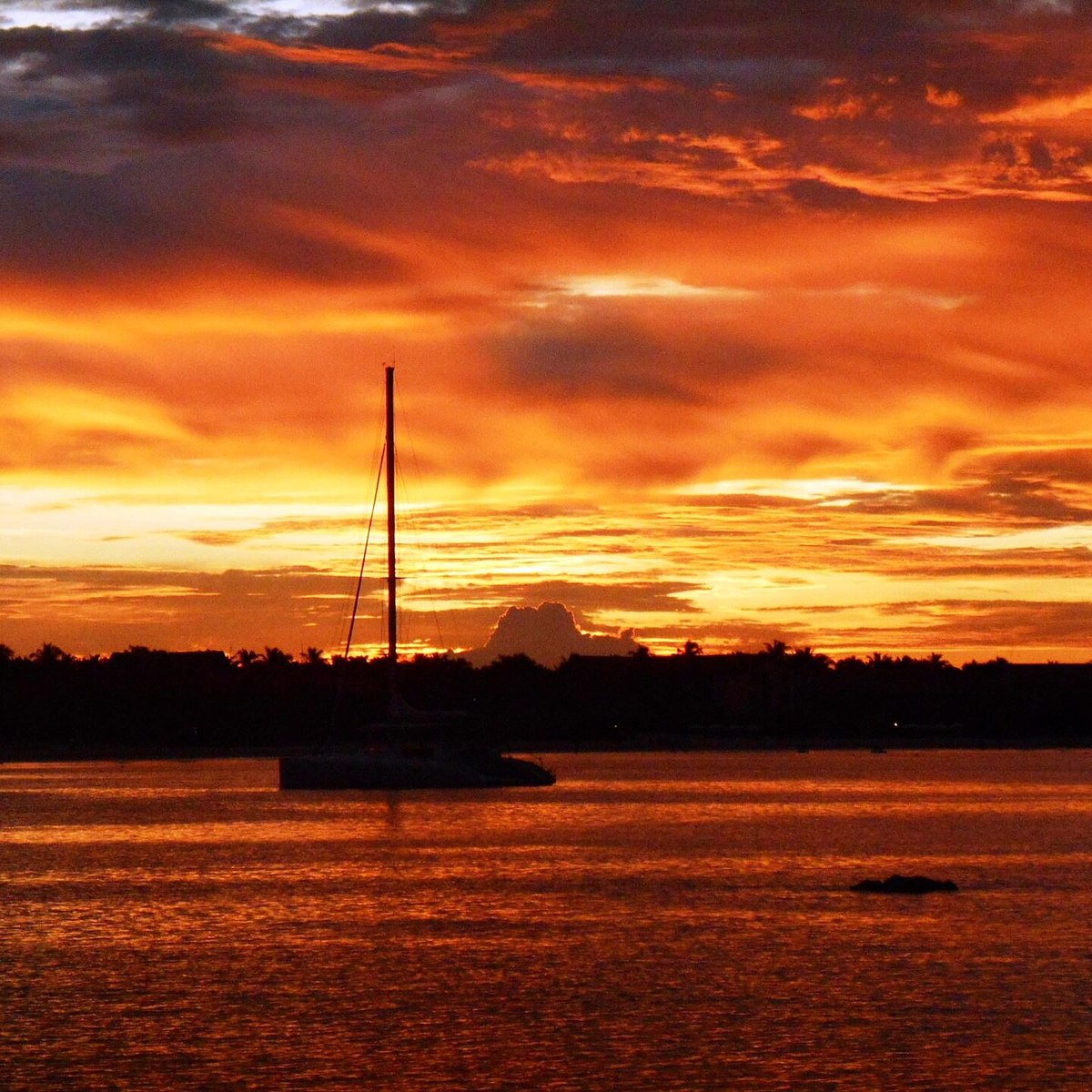 An orange sunset over the water with a yacht anchored in silhouette